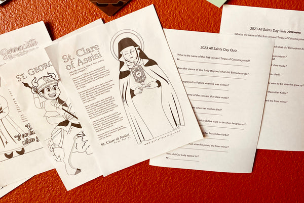 A collection of printed Saint Trivia Game materials, including coloring pages with illustrations of saints and trivia quiz sheets, laid out on a surface.